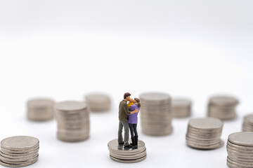 Money, Financial, Business and Family concept. Parent man, woman and kid Miniature figures hug and kiss and standing on top of stack of silver coins with many stack on white background.