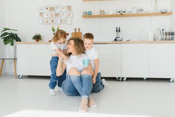 Happy young family, mom with little children sit on warm wooden floor in new modern design kitchen, mother with excited small kids relax rest in own renovated apartment, moving concept