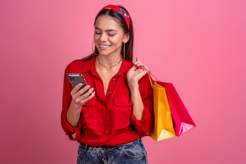 hispanic beautiful woman in red shirt smiling holding holding shopping bags and smartphone
