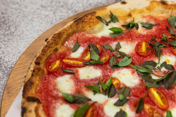 Margherita Pizza with Basil and Rustic Tomato Sauce Homemade Artesanale Close Up Detail on a Round Wooden Plate with Flour Background Table