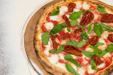 Pizza Aragula and Sun Dried Tomatoes Homemade Artesanale Close Up Detail on a Round Wooden Plate with Flour Background Table