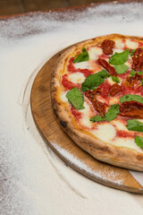 Pizza Aragula and Sun Dried Tomatoes Homemade Artesanale Close Up Detail on a Round Wooden Plate with Flour Background Table