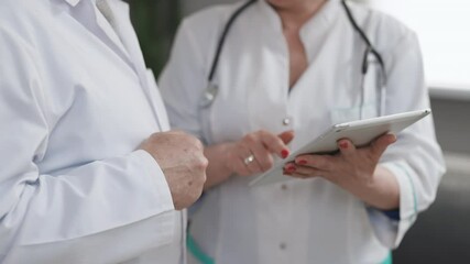 Closeup view of man and woman doctors using tablet during working day at clinic. Caucasian person and his female colleagues use electronic device and work together while standing indoors.