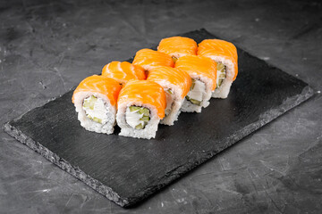 appetizing philadelphia sushi roll with salmon and cucumber on a black stone plate