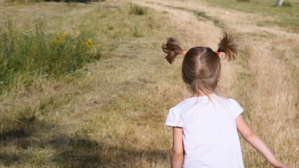 Toddler girl back running bu countryside road. Child with blonde ponytails jumping