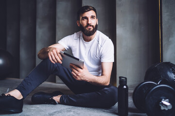 Athletic male sitting with tablet on floor in gym