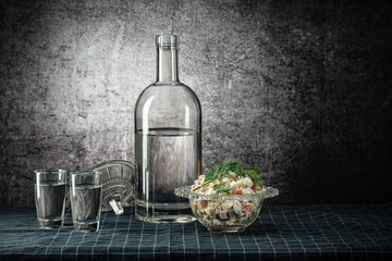A bottle and two glasses, with a strong drink, and an olivier salad, on a dark tablecloth, on a background with a stain