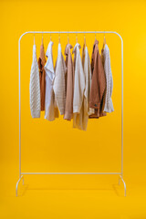 Studio vertical shot of white minimalistic rack with wooden hangers and light colored clothes, isolared on bright colored yellow background