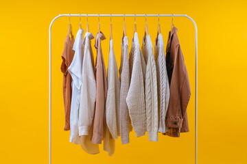 Studio shot of casual cozy light-colored female clothing hanging on white rack, isolated on yellow background