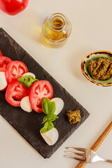 Traditional Italian caprese salad with mozzarella, tomatoes, basil and olive oil on dark plate.  Capreze still life, top view
