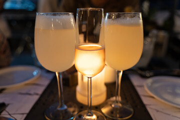 Glass of rose wine between pisco sour big glasses with candle light behind. Fancy restaurant diner, drink celebration concepts