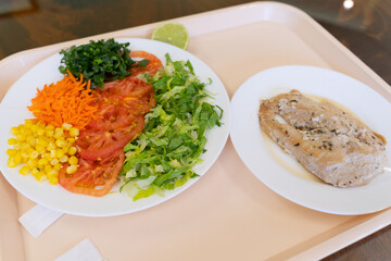Factory menu tray with salad of lettuce, tomato, corn, carrot and chicken steak. Lunch break concept