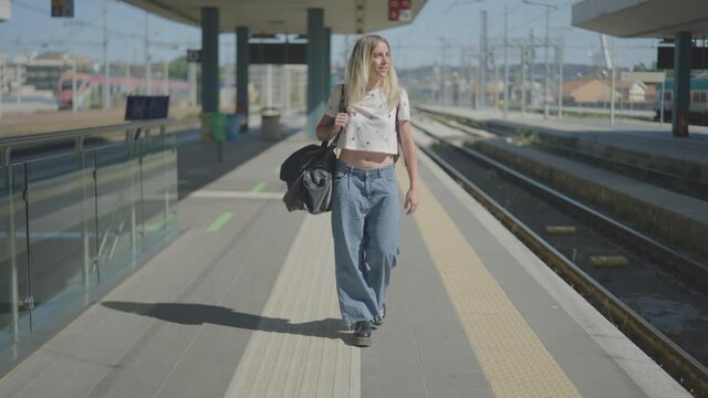 Steady shot of an attractive young woman at the rail station's train track ready to leave for a holiday, vacation, or Erasmus project in summer.