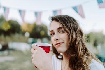 Chica joven con vaso rojo sentada junto a una caravana con la bandera de estados unidos de america bebiendo algo
