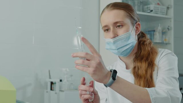 young nurse trainee holding a large syringe with medicine and examining a syringe. The medical practitioner looks at the syringe with the drug