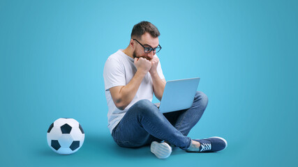 Portrait of casually dressed bearded man watching football play live broadcast on his laptop, making bets online at bookmaker's website, feeling nervous waiting for the final score
