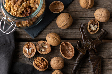 Obraz na płótnie Canvas Tasty walnuts with cracked split nutshells, jaw and dragon nutcracker on rustic napkin and wood table. top view