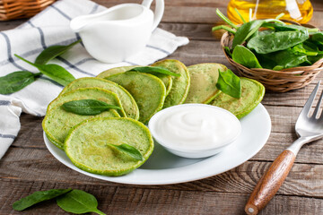 Spinach pancakes with spinach leaves and sour cream on a table. Gluten free spinach pancakes recipe