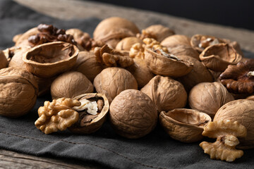 Tasty walnuts with cracked split nutshells on rustic napkin and wood table