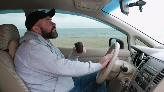 Male driver driving a car, holding a cup of coffee and looking relaxed in front of