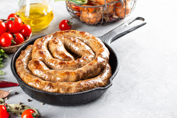 Spiral grilled sausage with spices in a frying pan on a stone background, copy space