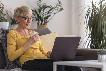 Beautiful senior elderly woman at home using laptop computer to communicate with her family,...
