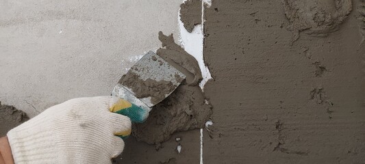 The hand of a white man in a glove and with a spatula putty on the wall. Construction and repair of premises.
