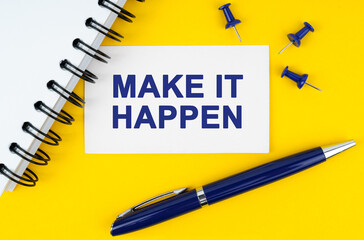 On a yellow background lies a notebook, a pen and a business card with the inscription - MAKE IT HAPPEN