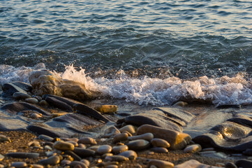 pebble stones on the sea beach, the rolling waves of the sea with foam