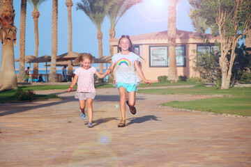 Happy sisters run on footpath in tropical resort