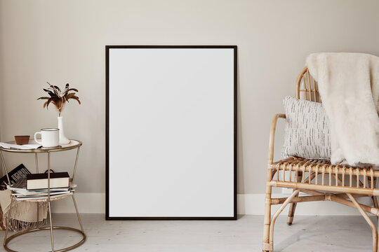 Large black thin frame poster mockup laying on the floor with bohemian style props and furniture. 