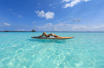 girl in bikini lies on Surfboard in the ocean, Maldives