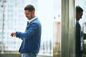 stylish guy smiles and looks at the clock on his hand standing on the street. photo with reflection. life style. plans his time