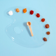 Various spices in a transparent painting palette and wooden spoon lay down against cyan background. Flat lay minimal creative concept