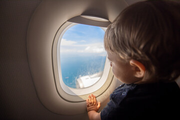 Fototapeta na wymiar Toddler looks at the ground through the porthole of a flying plane