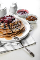 Vertical shot a stack of delicious hot pancakes with chocolate and raspberry jam. Traditional delicious dessert or sweet breakfast on a white plate on a light table. Food still life