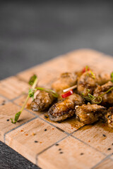 Fried mussels with chili, garlic, sesame, herbs, on square wooden board on gray background.