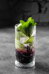 Cocktail with tonic, currant syrup, lime, mint, ice in tall glass on gray background. Puff cold drink with blueberries.