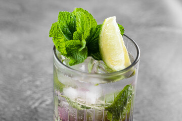 Cocktail with tonic, currant syrup, lime, mint, ice in tall glass on gray background. Puff cold drink with blueberries.