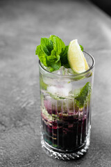 Cocktail with tonic, currant syrup, lime, mint, ice in tall glass on gray background. Puff cold drink with blueberries.