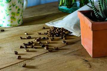 A background of black, roasted coffee beans scattered on a wooden table with plants alongside