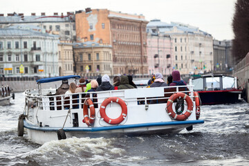 Flat vessel with tourists floats on water of the Fontanka river. Travel on water for seeing beautiful places and enjoy city's unforgettable view. Saint-Petersburg, Russia