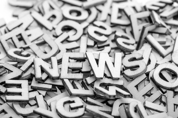 The word "news" is composed of little wooden letters and randomly letters in a pile on a white background. An abstract idea that will be proven in motivational words. B&W photo.