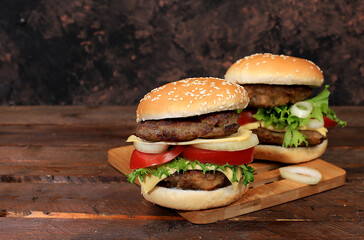 Two double cheeseburgers with fresh lettuce leaves, tomatoes, cream cheese, onion and cutlet on an old wooden board, food delivery, cafe, restaurant, menu,