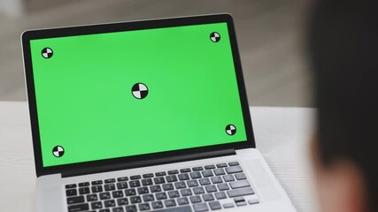 Back view of businessman look green screen laptop in office. Close up shot of modern chroma key green screen laptop computer set up for work on desk at day - remote work, technology concept