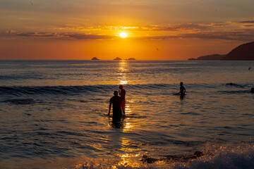 Pessoas assistem, dentro do mar, pôr do sol na Praia de Ipanema, Rio de Janeiro, Brasil