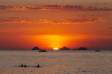 Fototapeta na wymiar Pessoas assistem, dentro do mar, pôr do sol na Praia de Ipanema, Rio de Janeiro, Brasil