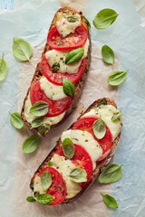 Grilled caprese sandwich based on sourdough bread with the addition of tomatoes, mozzarella cheese, fresh basil and olive oil on a light background top view