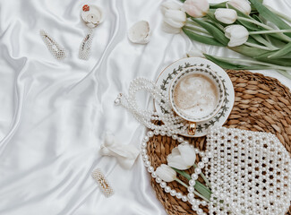 Female spring background, still life composition with coffee cup, candle, tulips, and woman accessory on silk background. womens holiday. Mothers Day. Womens Day.