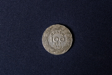 An old hundred reis coin dated 1940 used in Brazil on a dark black background with light from left to right. Illustrative details on the outer circumference.